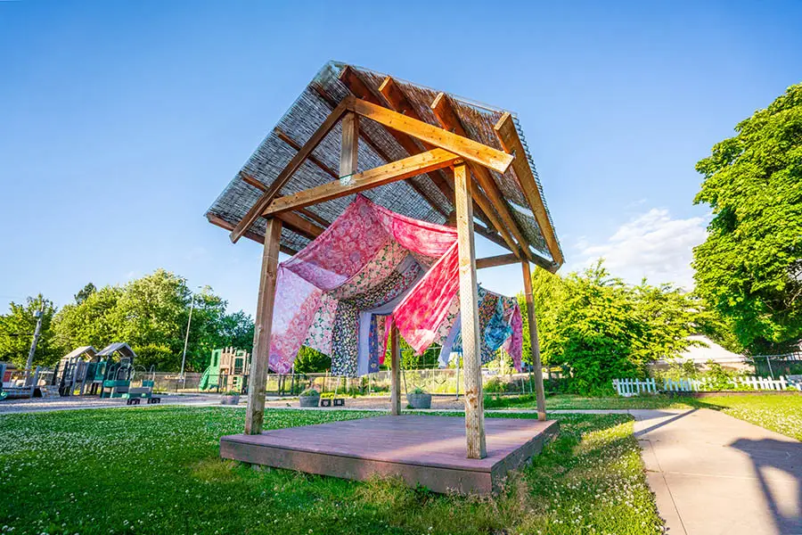 The image shows a gazebo in the outdoor play area of Chemeketa's Child Development Center. There are several colorful fabric banners hanging from the structure, which add vibrant splashes of color against the natural background. No people are visible in the image, and there is no text present.